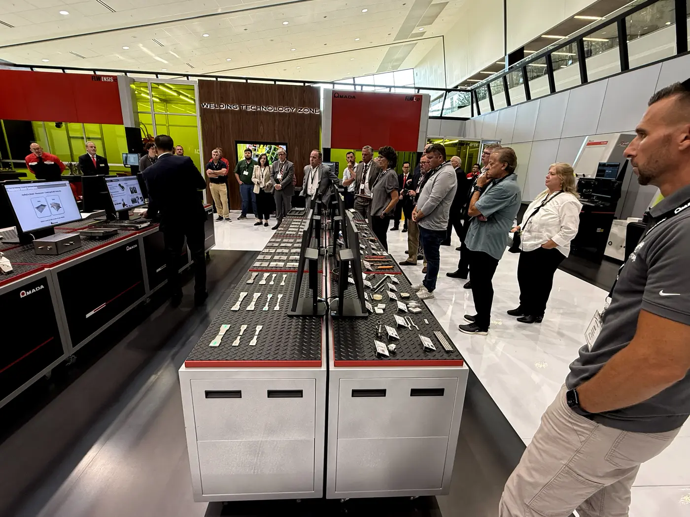 Visitantes revisando piezas de muestra soldadas en la mesa de exhibición